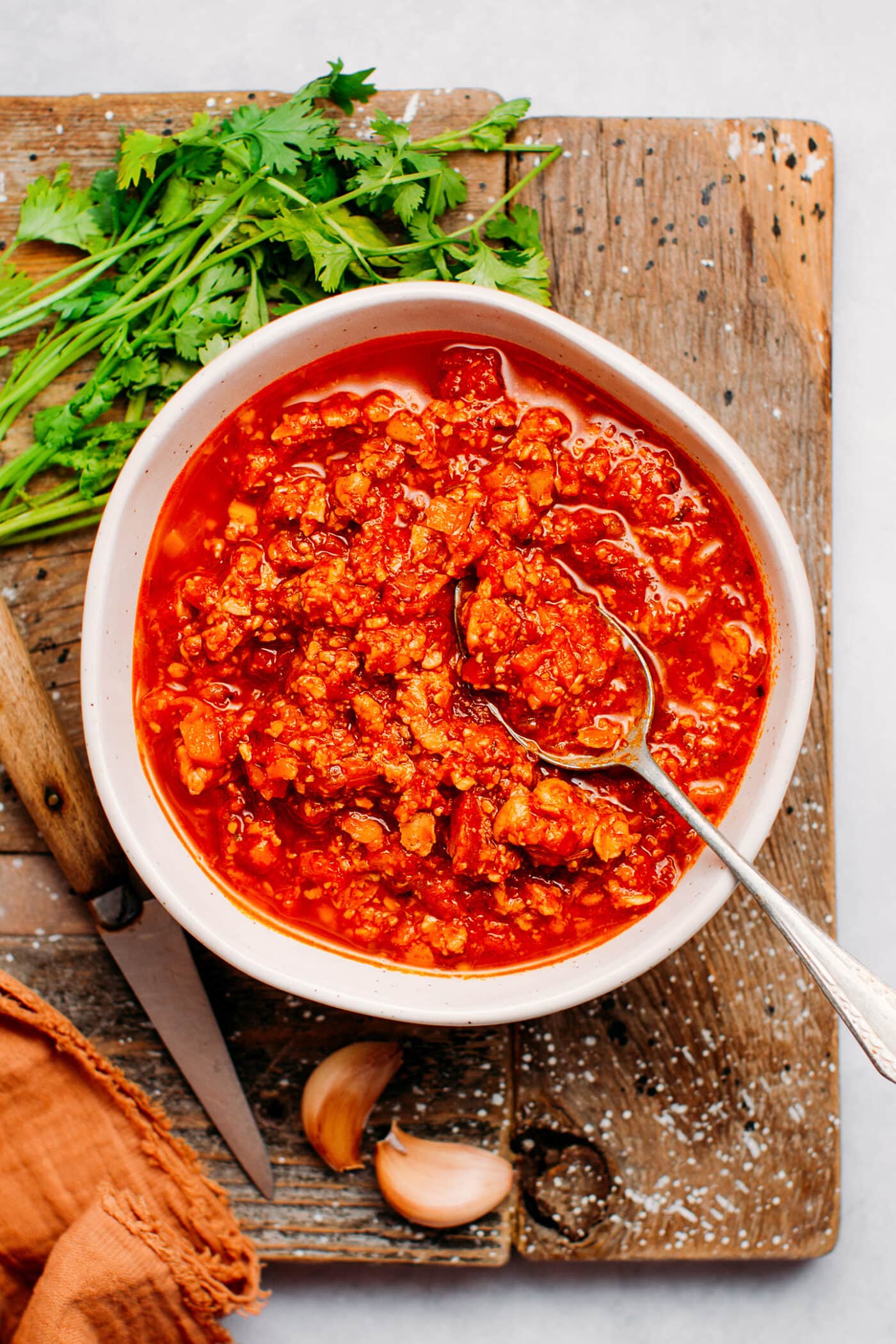 Tempeh bolognese in a bowl, on a cutting board.