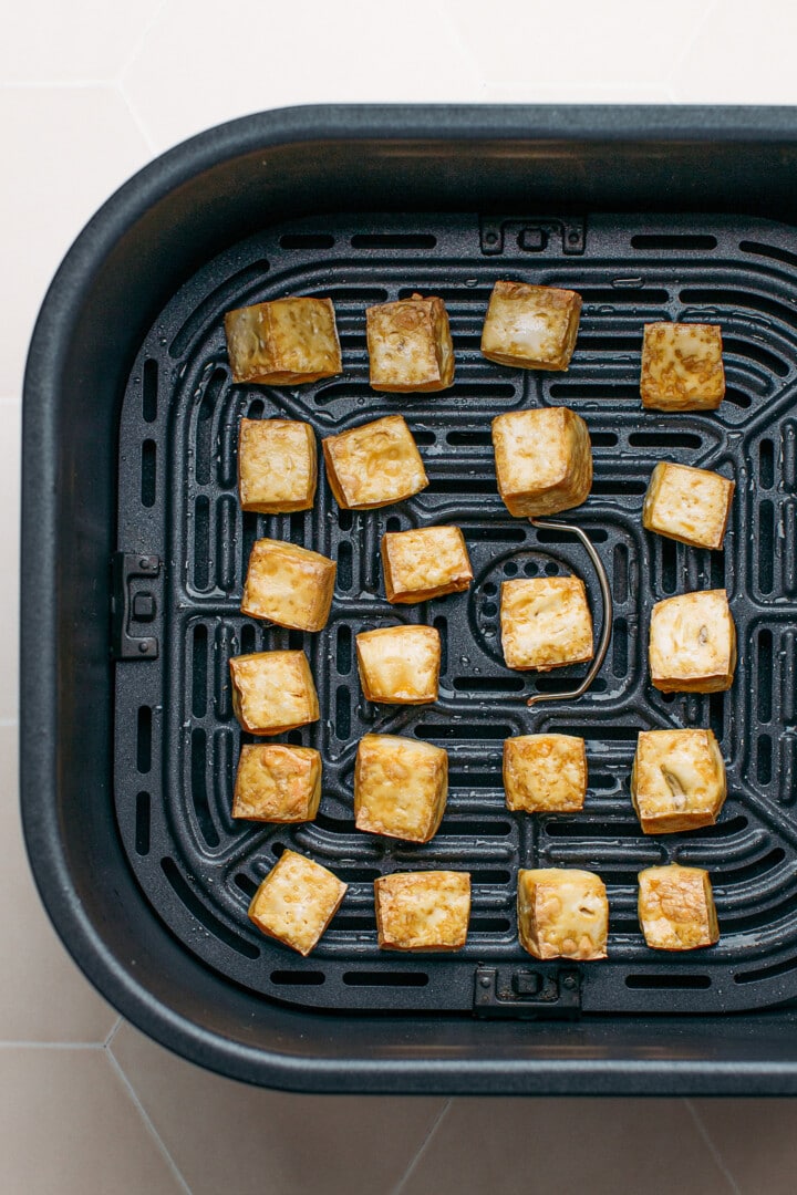 Air-fried tofu in the basket of an air fryer.