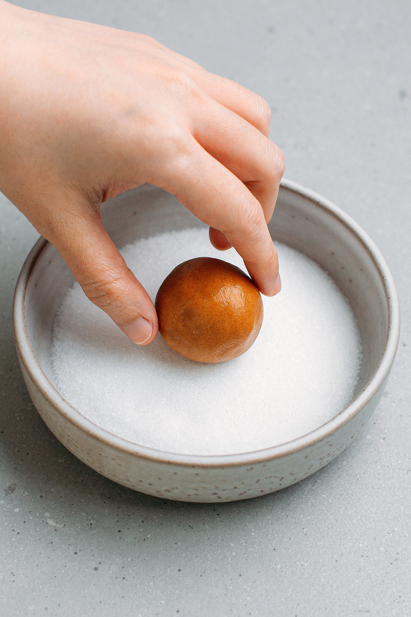 Rolling a ball of cookie dough in granulated sugar.