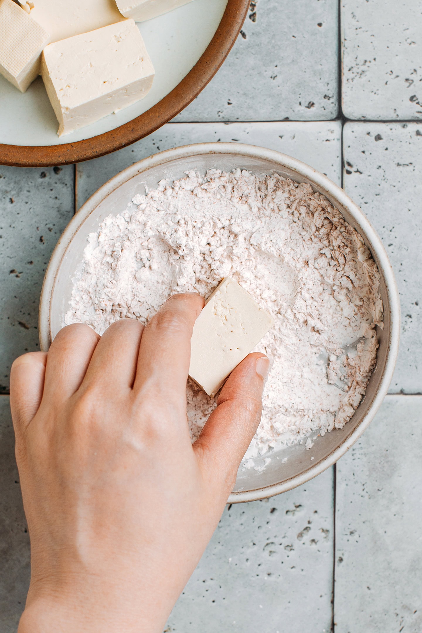 Adding a cube of tofu to a bowl of cornstarch.