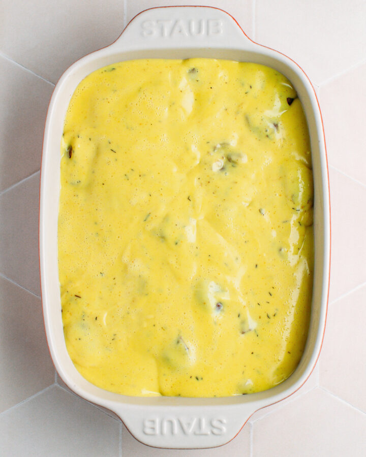 Vegan cream poured over parsnips, carrots, and chestnuts in a baking dish.