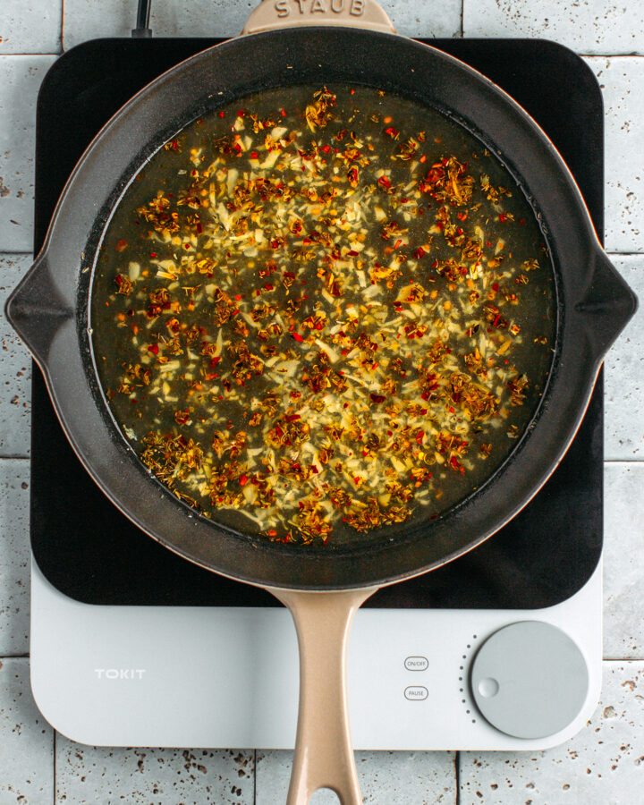 Sautéed garlic and vegetable broth in a skillet.