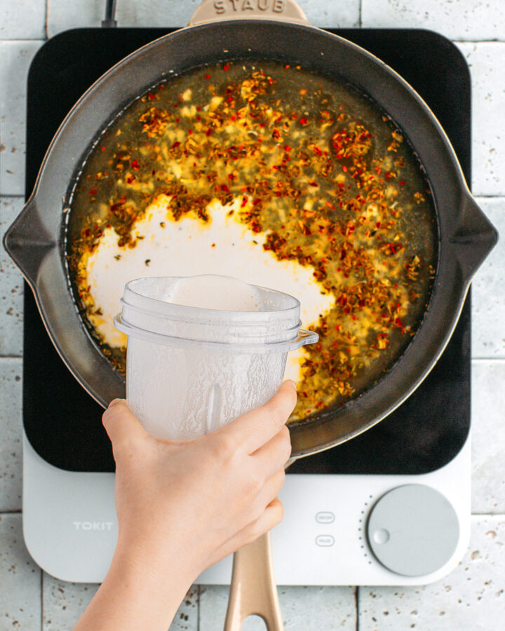 Pouring cashew cream in a skillet containing vegetable broth.