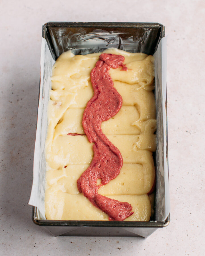 Swirl of strawberry batter on top of vanilla cake batter in a loaf pan.