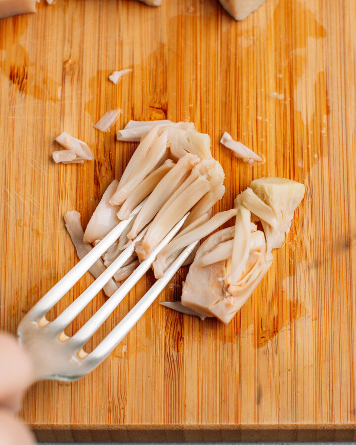 Shredding a piece of young green jackfruit using a fork.