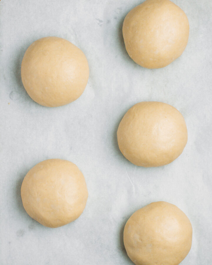 Five balls of dough, after rising, on a baking sheet.