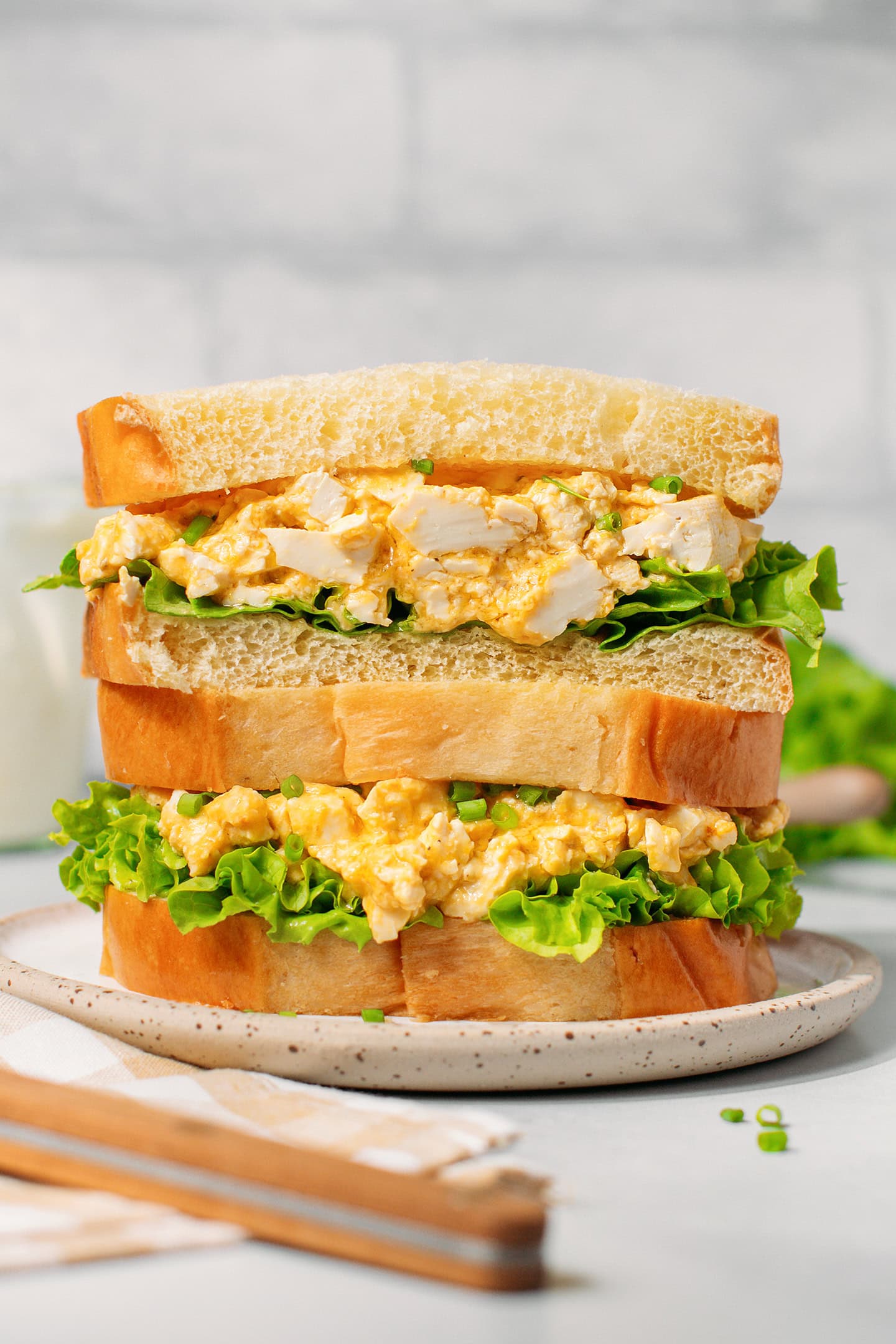 Two egg salad sandwiches stacked on a small white plate.