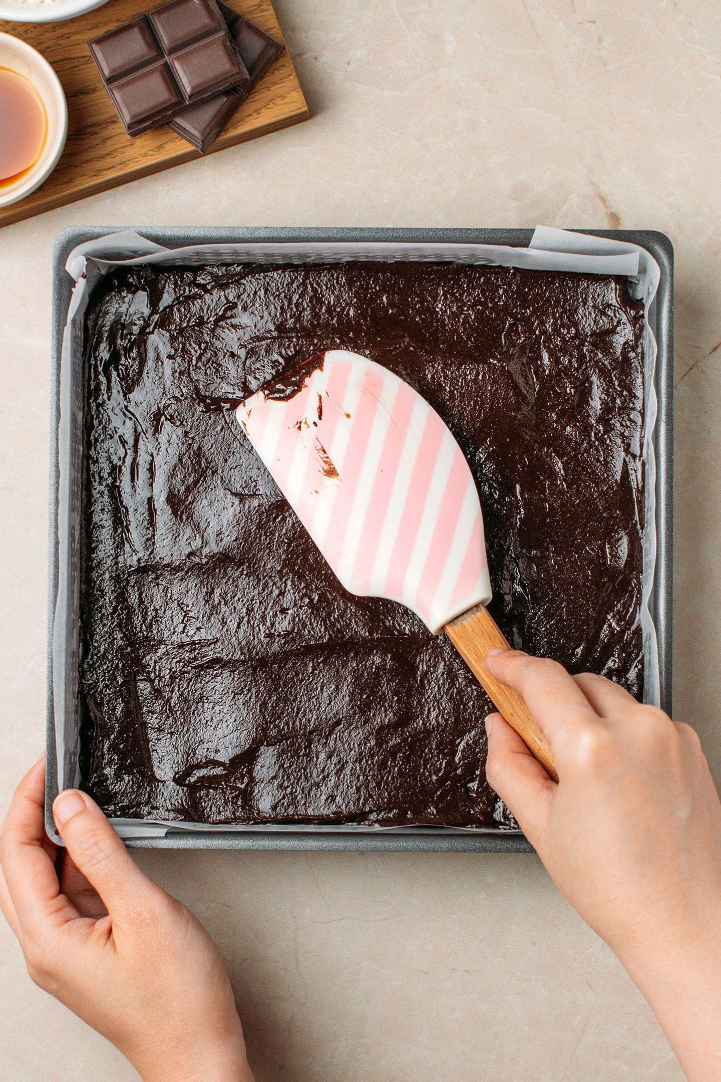 Using a spatula to spread brownie batter in a pan.
