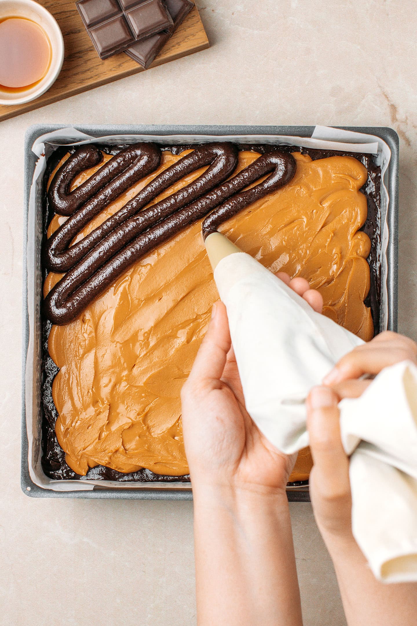 Piping brownie batter over a layer of peanut butter.