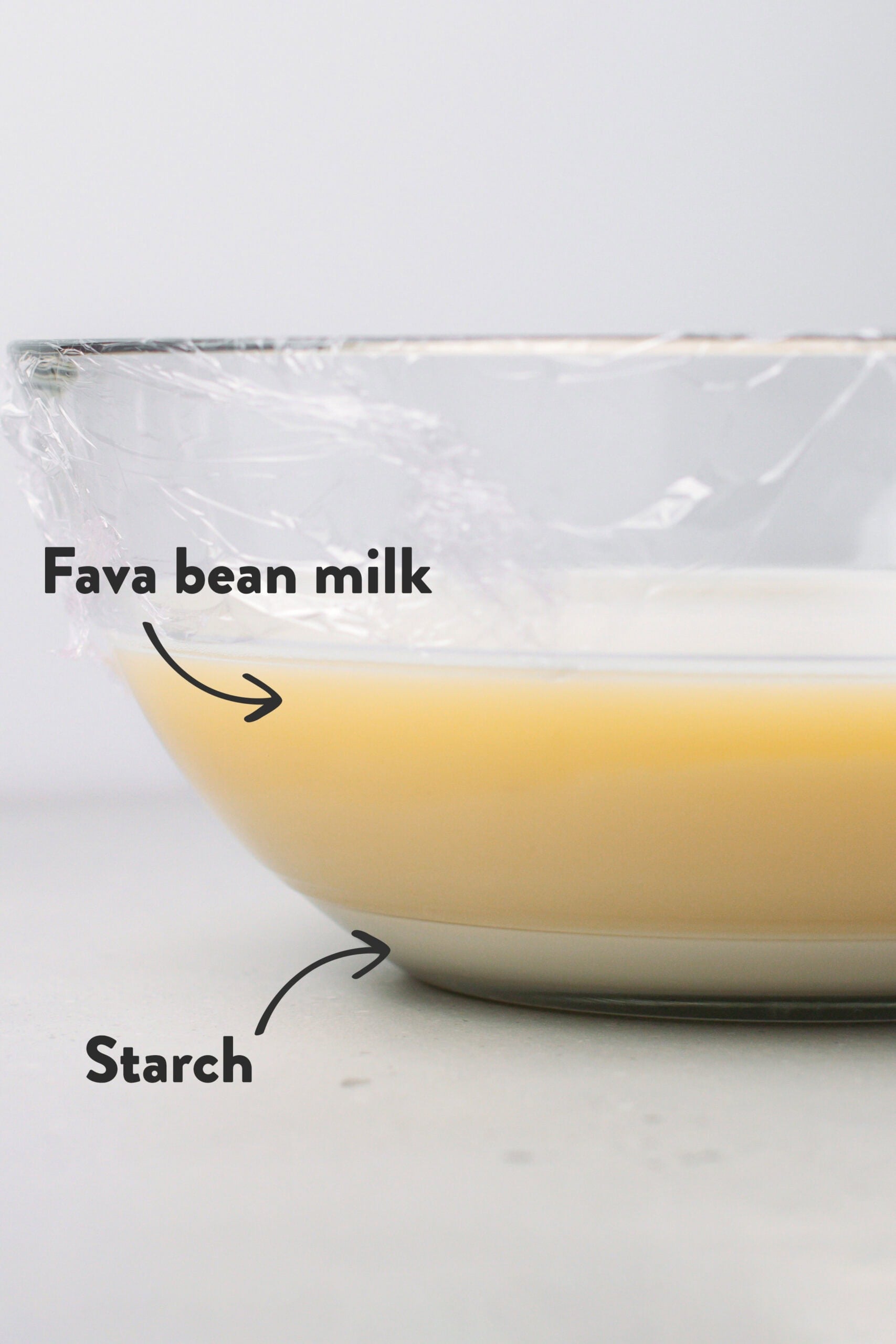 Glass bowl showing fava bean milk and starch at the bottom.