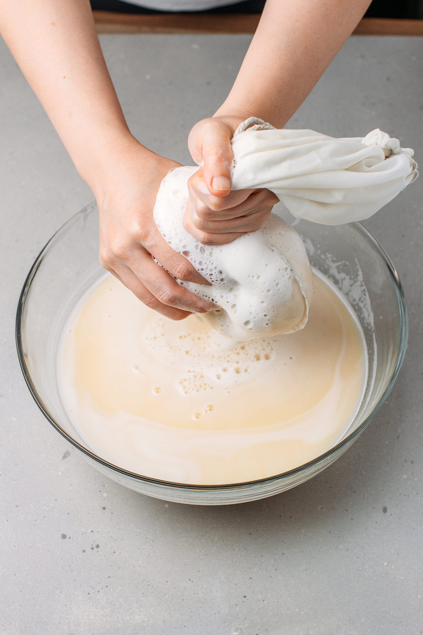 Squeezing a nut milk bag over a mixing bowl to squeeze out milk.
