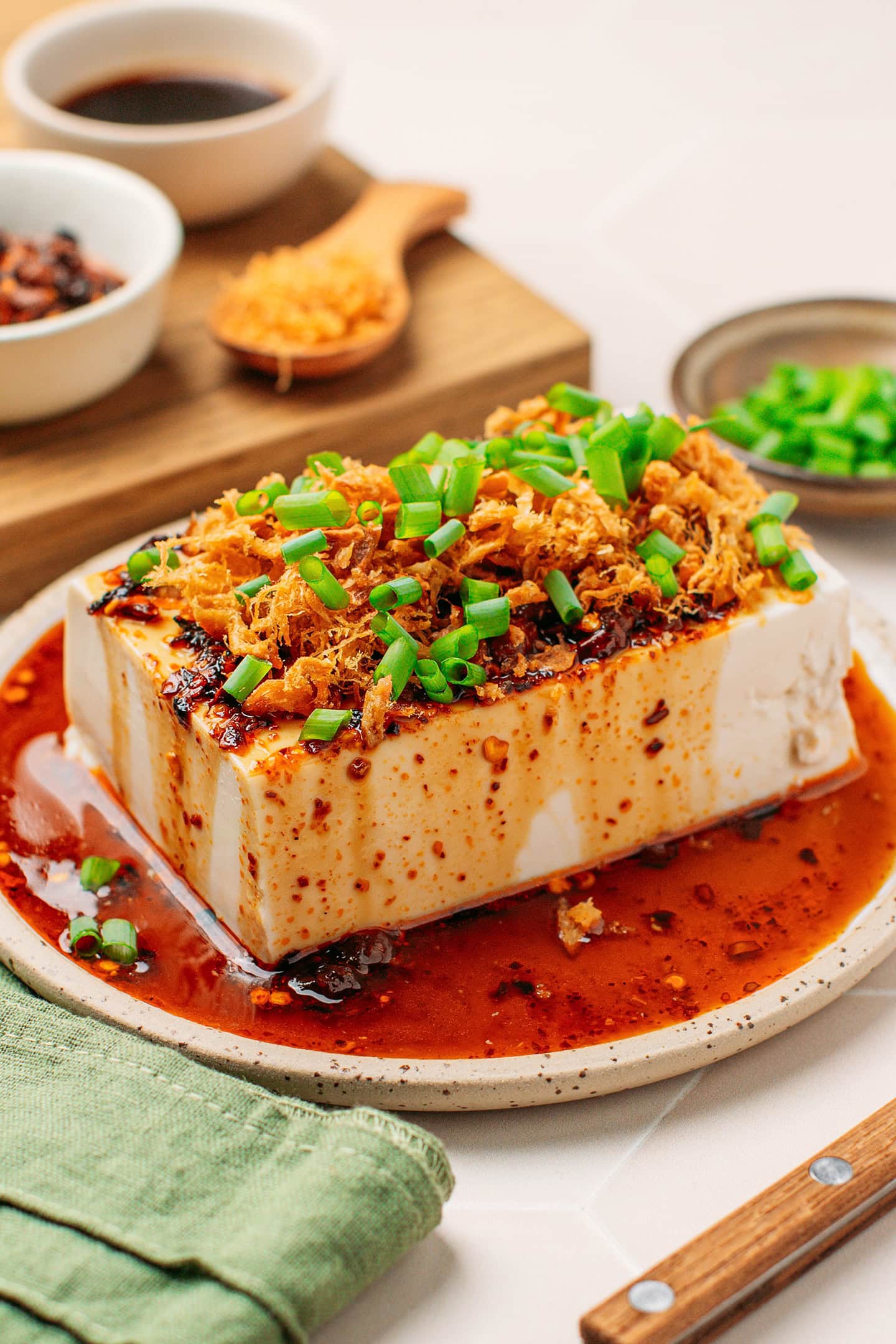 Block of silken tofu coated with chili crisp sauce and garnished with vegan meat floss and green onions.