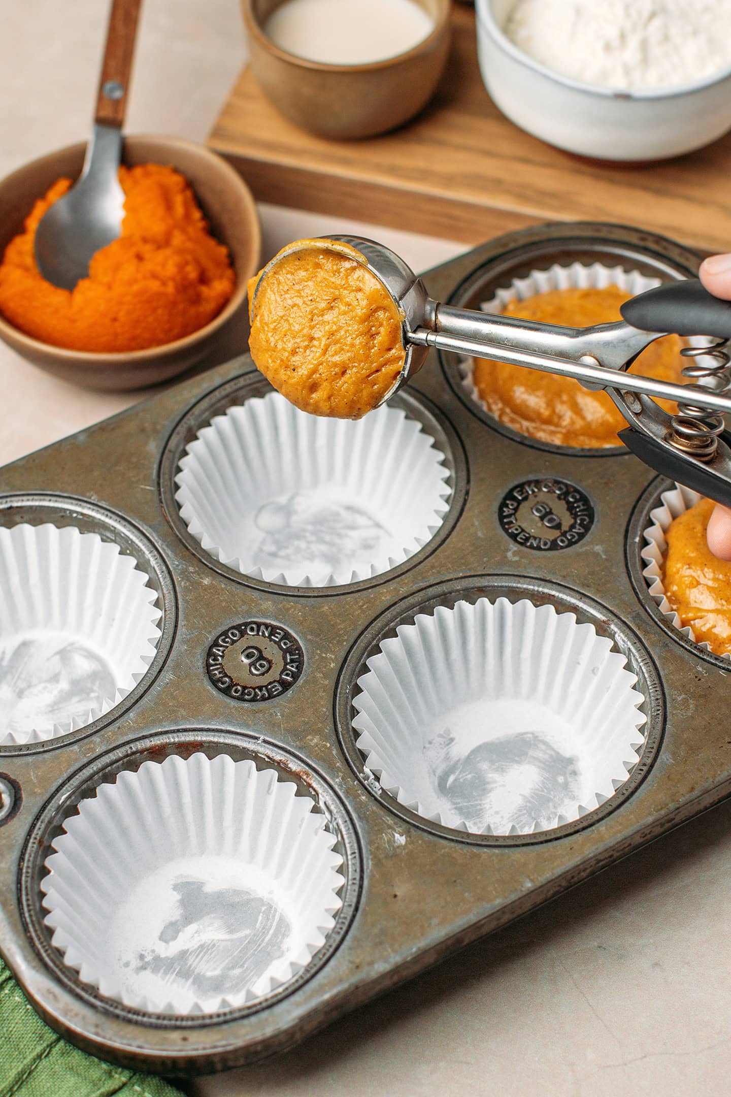Using a cookie scoop to fill a muffin pan with batter.